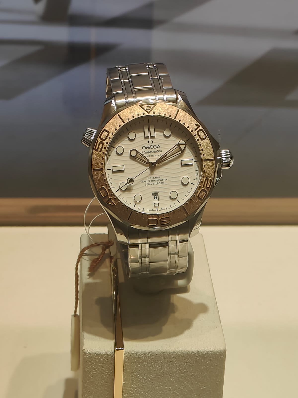Vitrinde beyaz dalga desenli kadranlı ve altın rengi bezelli güncel bir Omega Seamaster Diver 300M